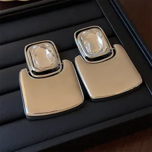Detailed macro view of exaggerated square metal stud earrings with clear crystals