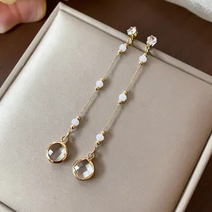 Dettaglio macro di eleganti orecchini lunghi pendenti in oro con perle bianche e vetro