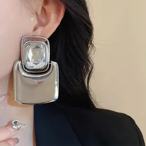 Close-up of exaggerated square metal earrings with large crystal inlay