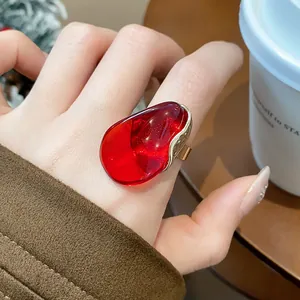 Detailed view of a bold red resin oval ring with elegant gold trim worn on a finger.