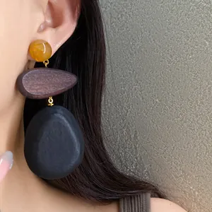 Detail view of large geometric ethnic style wood and resin dangle earrings worn on ear.