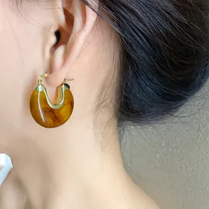 Detail view of amber resin geometric hoop earring on model, stylish retro jewelry.