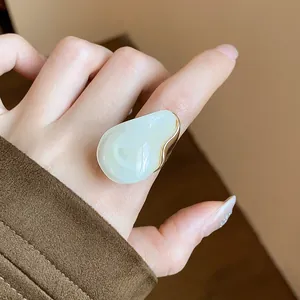 Detailed close-up of a chunky white teardrop resin ring with gold trim on finger
