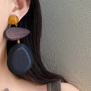 Close-up detail of ethnic wood drop earrings with amber resin and black stone-like pendant
