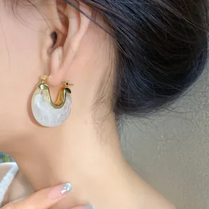 Close-up of white marble resin geometric hoop earrings with gold finish