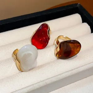 Close-up detail of stylish oval resin rings in red, white and amber with gold adjustable bands