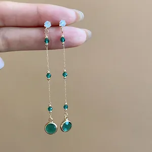 Vista dettagliata di eleganti orecchini lunghi con vetro verde e catena dorata.
