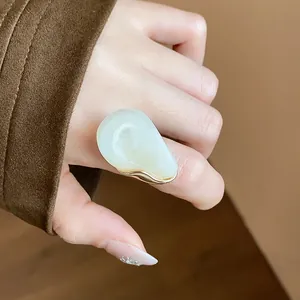 Detailed view of a chunky milky white resin open ring with gold trim on model's hand