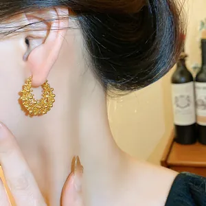 Detailed macro view of textured 18k gold-plated hollow hoop earring on model's ear