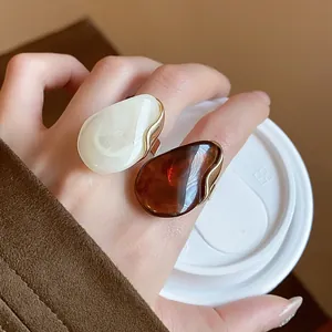 Close-up of chunky resin oval open rings in amber and white on woman's index finger.