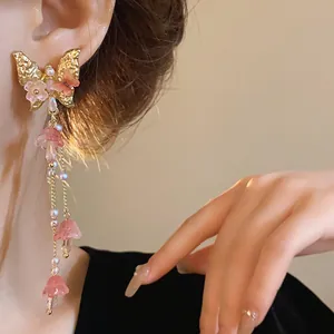 Close-up of elegant gold butterfly earrings featuring pink crystal flower tassels.