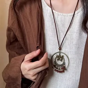 Collana lunga etnica con ciondolo a farfalla e nappe di piume marroni su abito in lino