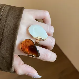 Close-up of oversized amber and white resin rings with gold-tone frames on hand