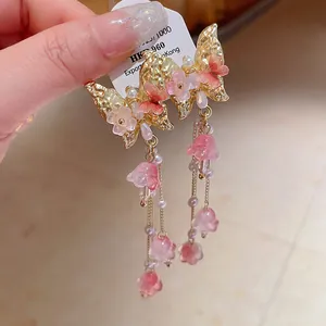 Close-up detail of golden butterfly earrings with delicate pink crystal flower tassels
