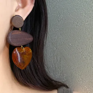 Close-up of vintage style wooden heart drop earrings featuring amber resin pendant