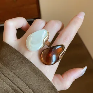 Close-up of two irregular resin rings in cream and amber worn on a hand.