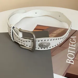 Close-up of white leather belt featuring silver studs and a vintage metal buckle detail