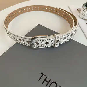 Detailed view of white faux leather belt with metal eyelets and shiny rhinestone studs.