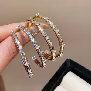 Detail showing elegant zircon stones and crisscross engraving on gold and silver hoop earrings