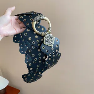 Close-up of black leather wide belt with bronze grommets and ornate round buckle