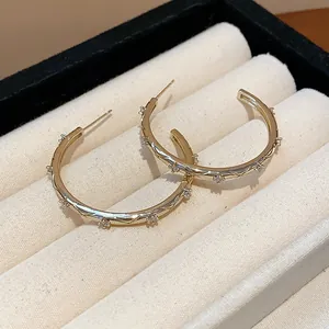 Close-up of gold-plated hoop earrings with sparkling zircon stones and cross pattern