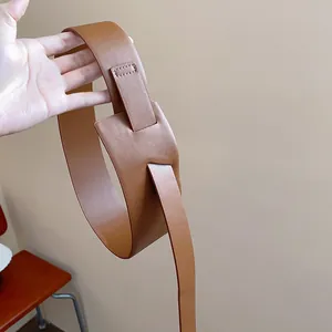 Close-up detail shot of a minimalist camel leather belt featuring a unique pass-through buckle.