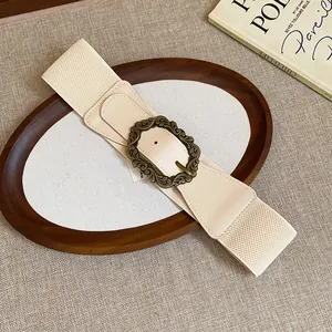 Detail view of the vintage bronze carved buckle on a stylish beige elastic wide belt