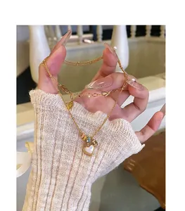 Detailed view of hand holding a gold-plated heart necklace with mother of pearl inlay