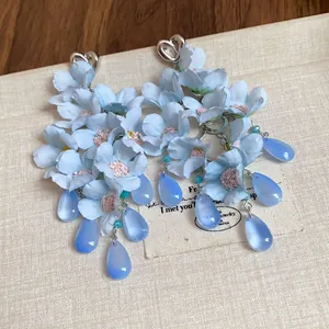 Dettaglio di orecchini a fiori in tessuto azzurro con pendenti a goccia di vetro