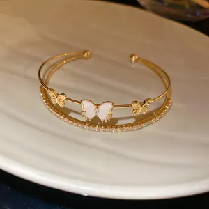 Primer plano detallado de un brazalete de oro de dos capas con circonitas y dijes de mariposa