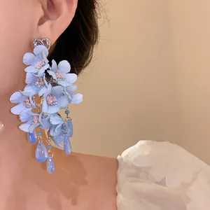 Dettaglio di orecchini a fiore in tessuto blu con nappine in vetro e perno a cuore argentato.