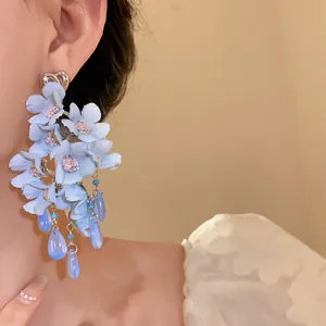 Primo piano di orecchini a fiore in tessuto blu con perni a cuore e nappe in vetro.