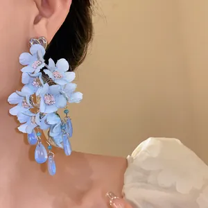 Primo piano elegante di orecchini a fiore blu con nappe di vetro indossati dalla modella