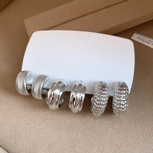 Detalle de un conjunto de pendientes de aro plateados con texturas sobre tarjeta