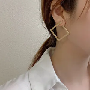 Detail of elegant gold geometric square hoop earrings worn by a model on a white shirt background.