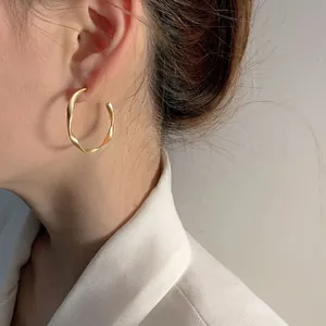 Close-up of a minimalist golden twisted hoop earring worn by a model in a white blazer