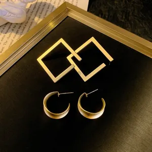 Detail view of geometric square interlocking earrings and gold hoop earrings on black background
