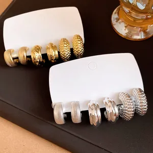 Detalle de juegos de pendientes en forma de C dorados y plateados texturizados.