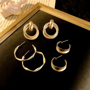 Detailed macro shot of various matte gold geometric hoop earrings with minimalist textures