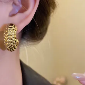 Primer plano de pendientes dorados con textura en forma de C usados por una modelo.