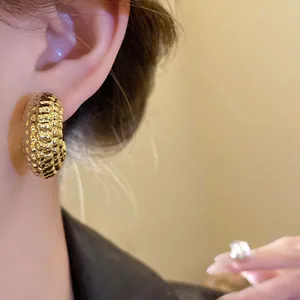 Vista detallada de pendientes de aro en forma de C dorados con textura de alta calidad