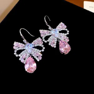 Close-up of elegant bow earrings with pink teardrop crystals and sparkling zircons.