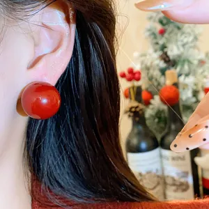 Primo piano di orecchini a sfera rossi indossati su sfondo con decorazioni natalizie