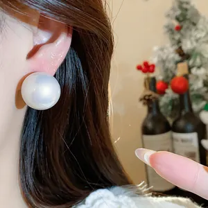 Primo piano di grandi orecchini a perla su modella con decorazioni festive di sfondo.