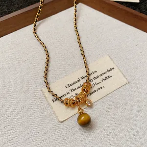Gros plan détaillé du pendentif en œil de tigre et des anneaux dorés sur le collier.