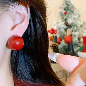 Eleganti orecchini a perno con perla rossa stile francese sul lobo con sfondo festivo.
