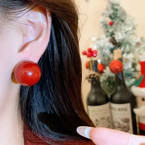Dettaglio di un orecchino a perno a sfera rossa minimalista indossato su sfondo festivo