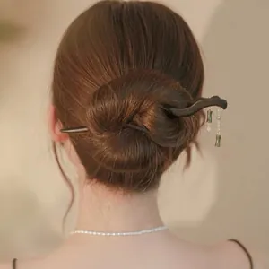 Detailansicht eines hölzernen Haarstabs mit grünen Bambusanhängern und weißen Perlen.