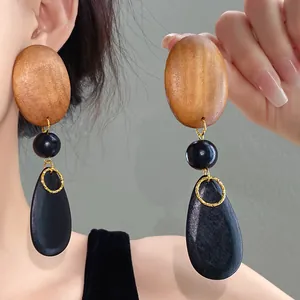 Detailed view of oversized wood bead and black teardrop dangle earrings on model