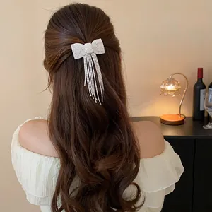 Elegant rhinestone bow hair clip with long tassels shown on a woman's wavy brown hair.